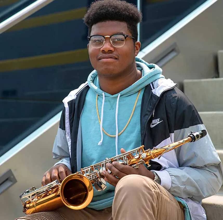 Young man, sitting holding saxophone on bleachers